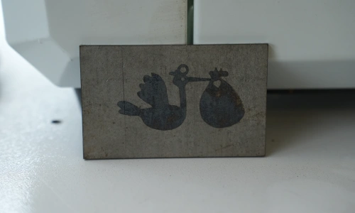 Laser-cut metal sample featuring two small decorative silhouette symbols