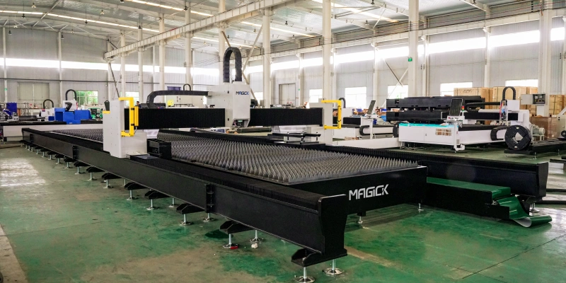 Front three-quarter factory view of the MAGICK MK-H large format laser cutting machine showing the long slat bed, gantry and ground rails